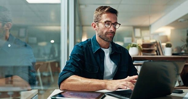 Man working on a laptop in a modern newsroom or office