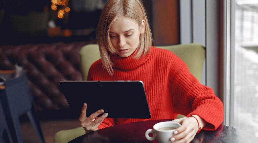 Woman reading on a tablet while holding coffee in a cozy café